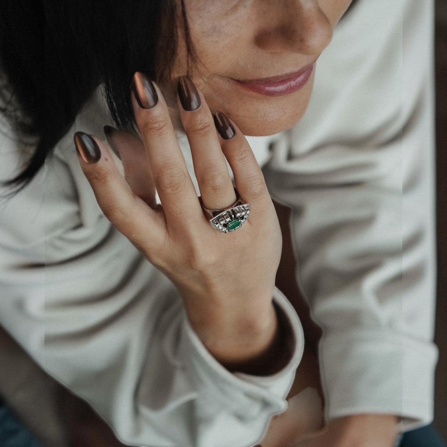 Menina Amsterdam 14K gold statement ring with a central emerald and diamond halo worn on a woman's finger