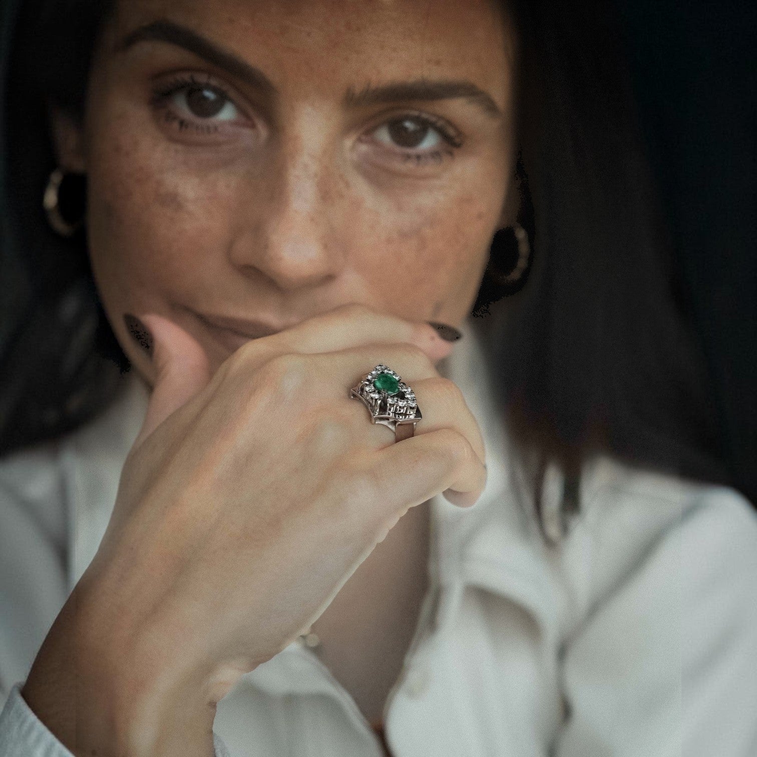 Menina Amsterdam Veyla statement ring in 14K gold with a central emerald and a geometric diamond halo on a woman's hand