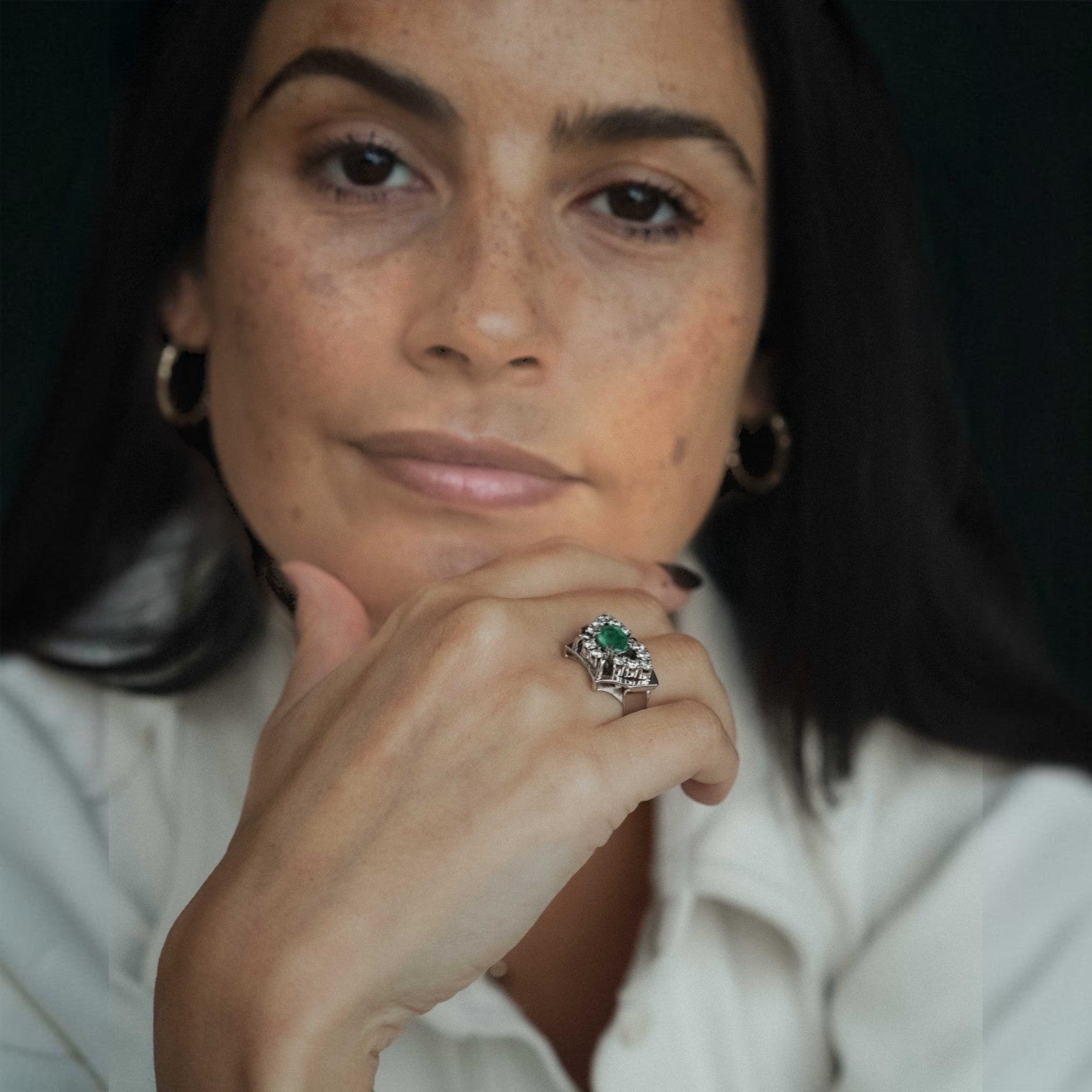 Menina Amsterdam Veyla statement ring featuring a central emerald and a diamond halo, worn by a woman