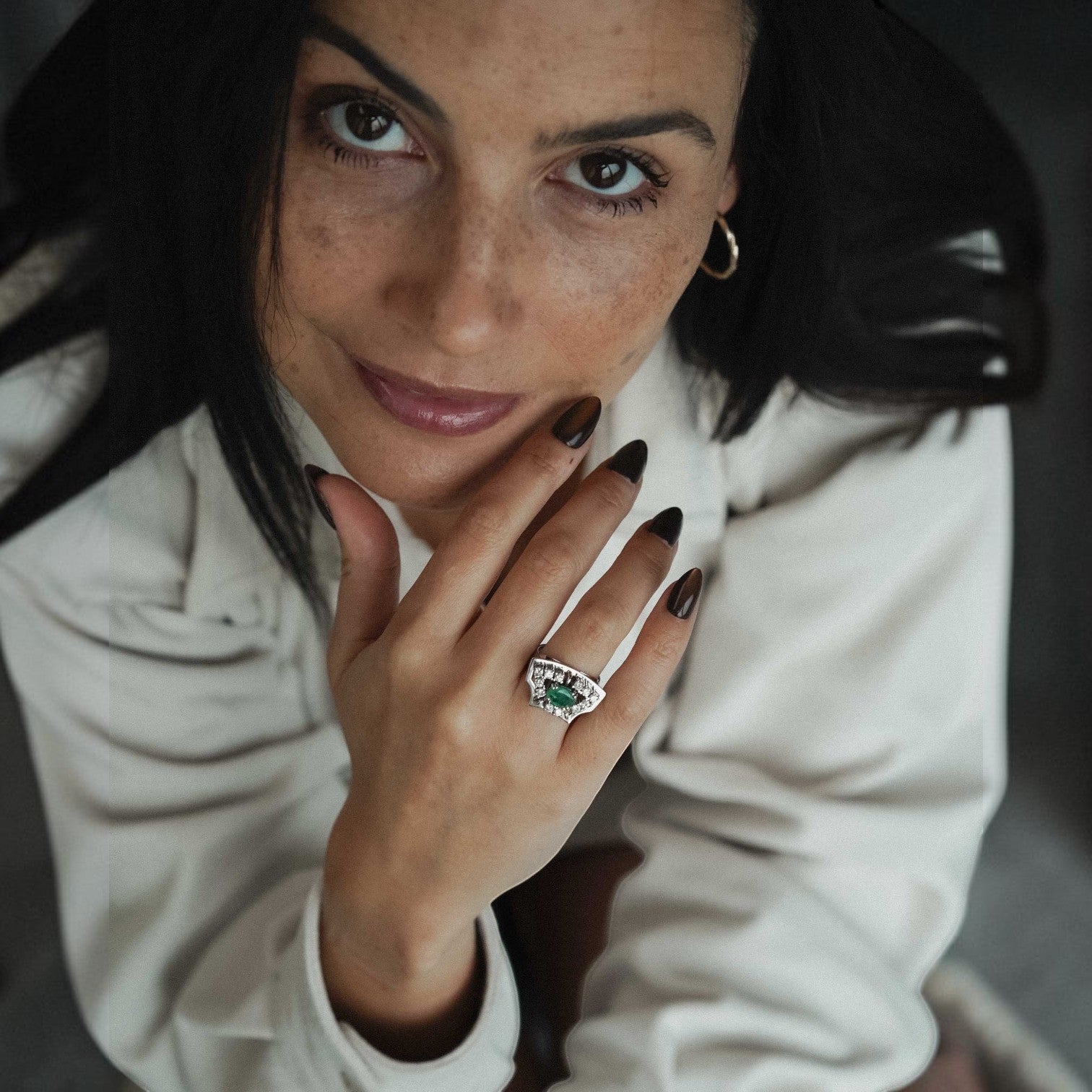Menina Amsterdam Veyla statement ring featuring a central emerald surrounded by brilliant-cut diamonds on a woman